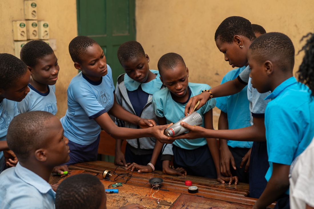 Pupils gathered around a device they have wired from a circuit board, speaker and battery